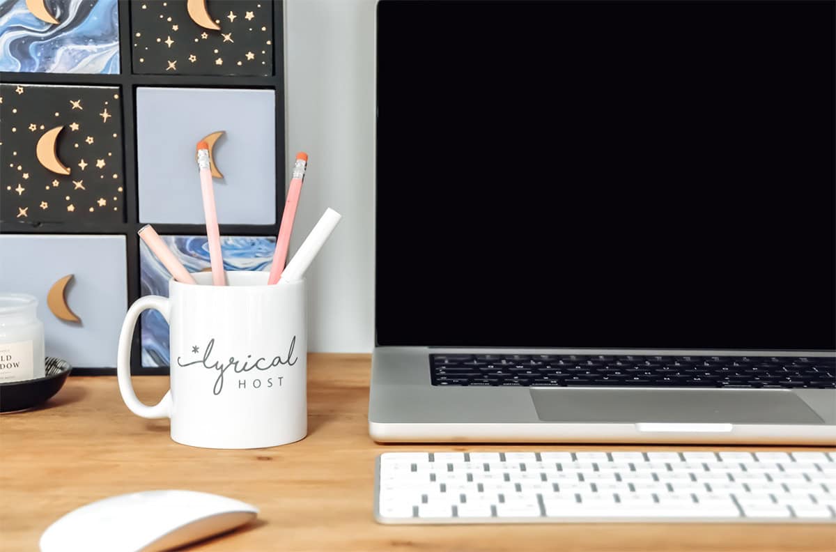 desk with laptop, lyrical host mug and other stationary